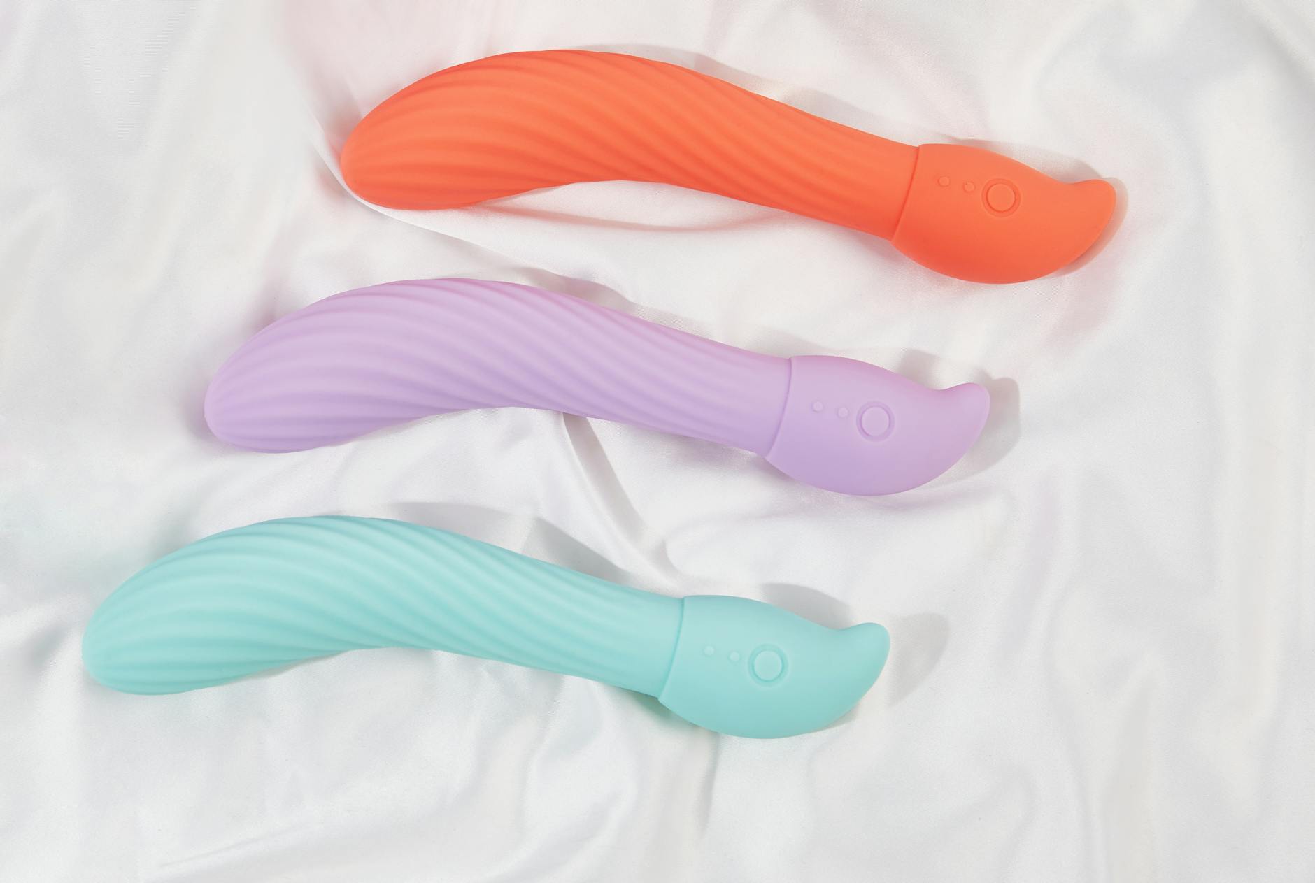 Three colorful silicone vibrators arranged on soft fabric, highlighting smooth textured design.