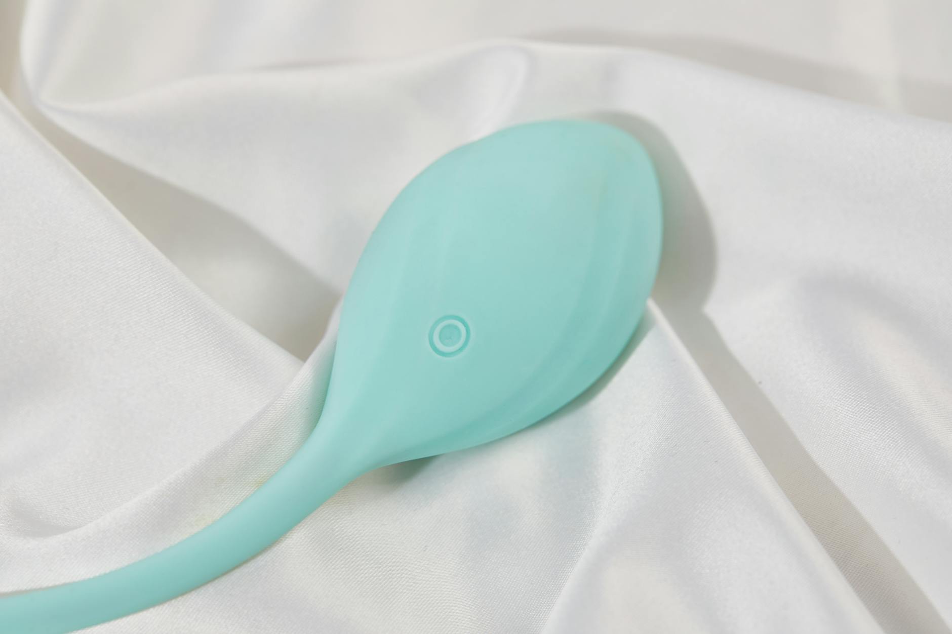A teal lemon-shaped clitoral vibrator on white silk fabric