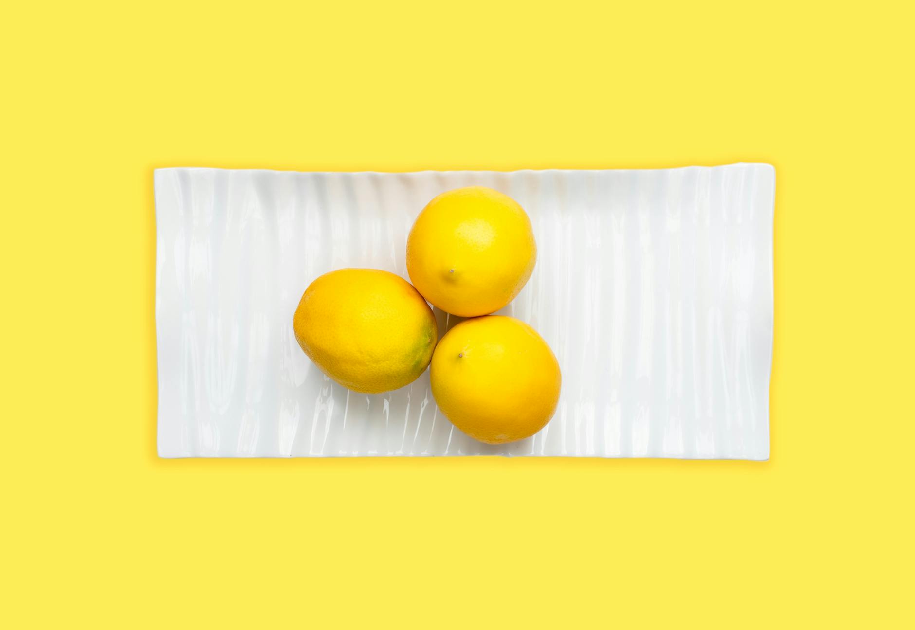 Fresh lemons on a white plate with vibrant yellow background, symbolizing renewal and fresh sensation