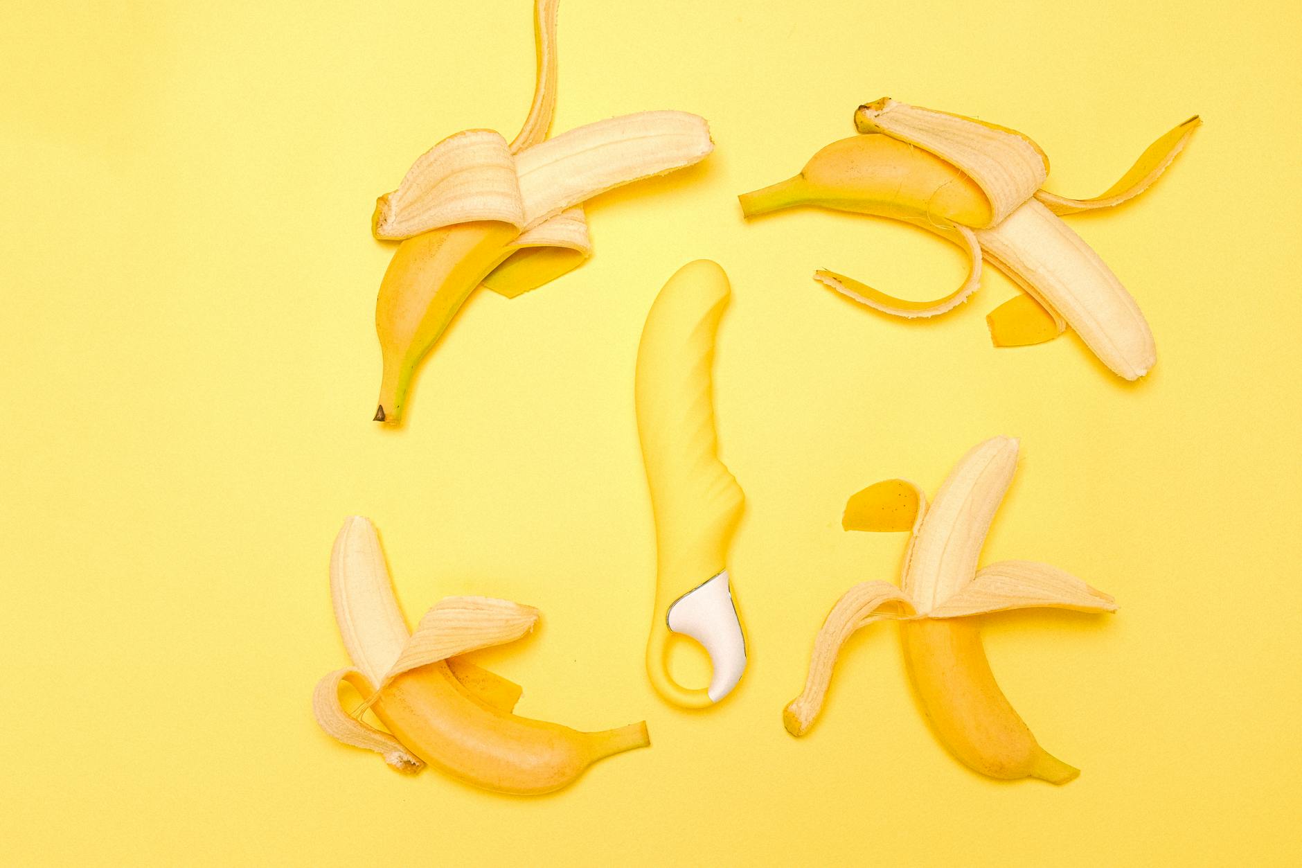A yellow silicone lemon vibrator surrounded by fresh lemons on a bright yellow background.