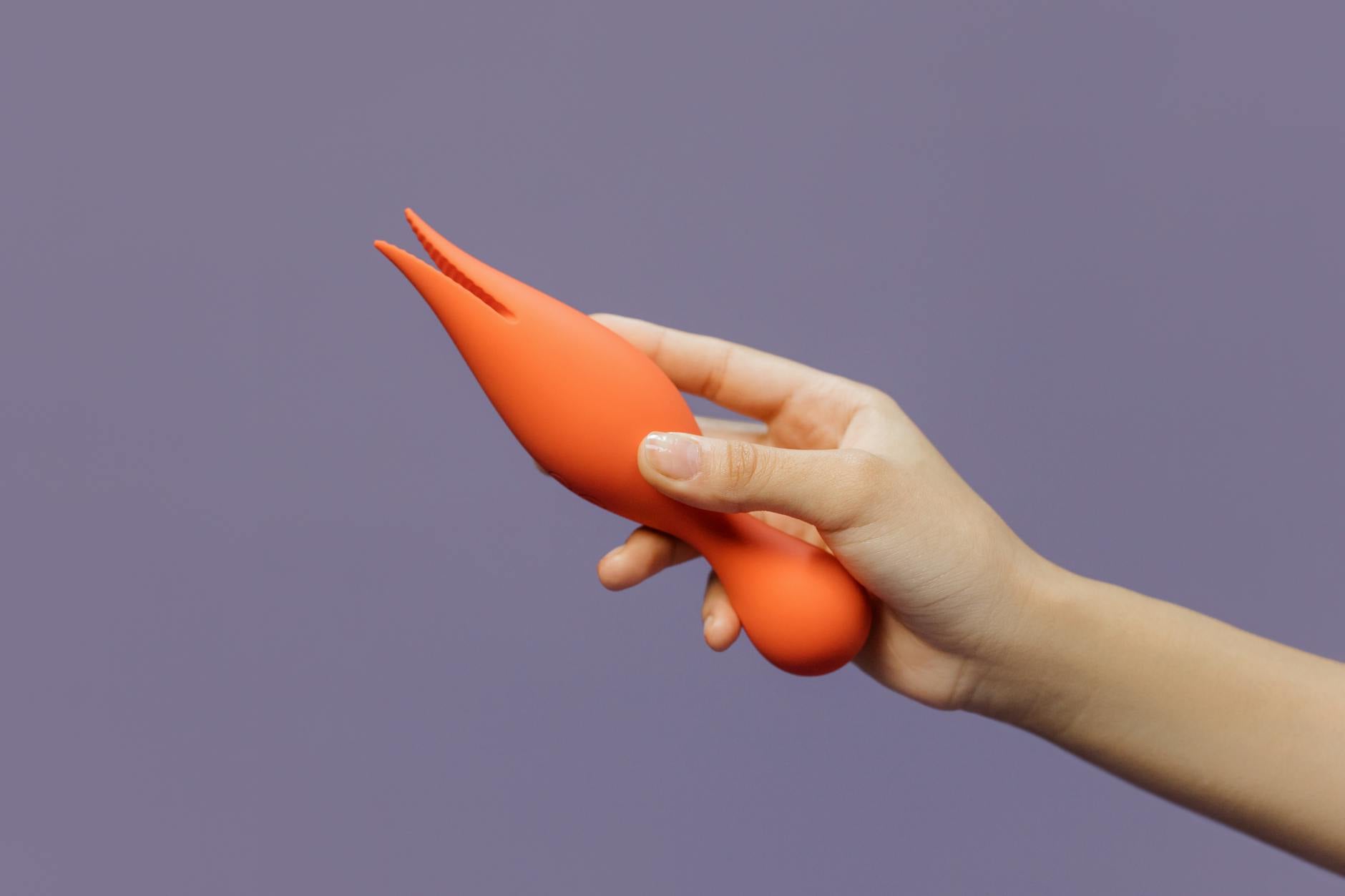 A close-up of a hand holding a vibrator against a minimalistic purple backdrop, showcasing modern sensuality and self-care.