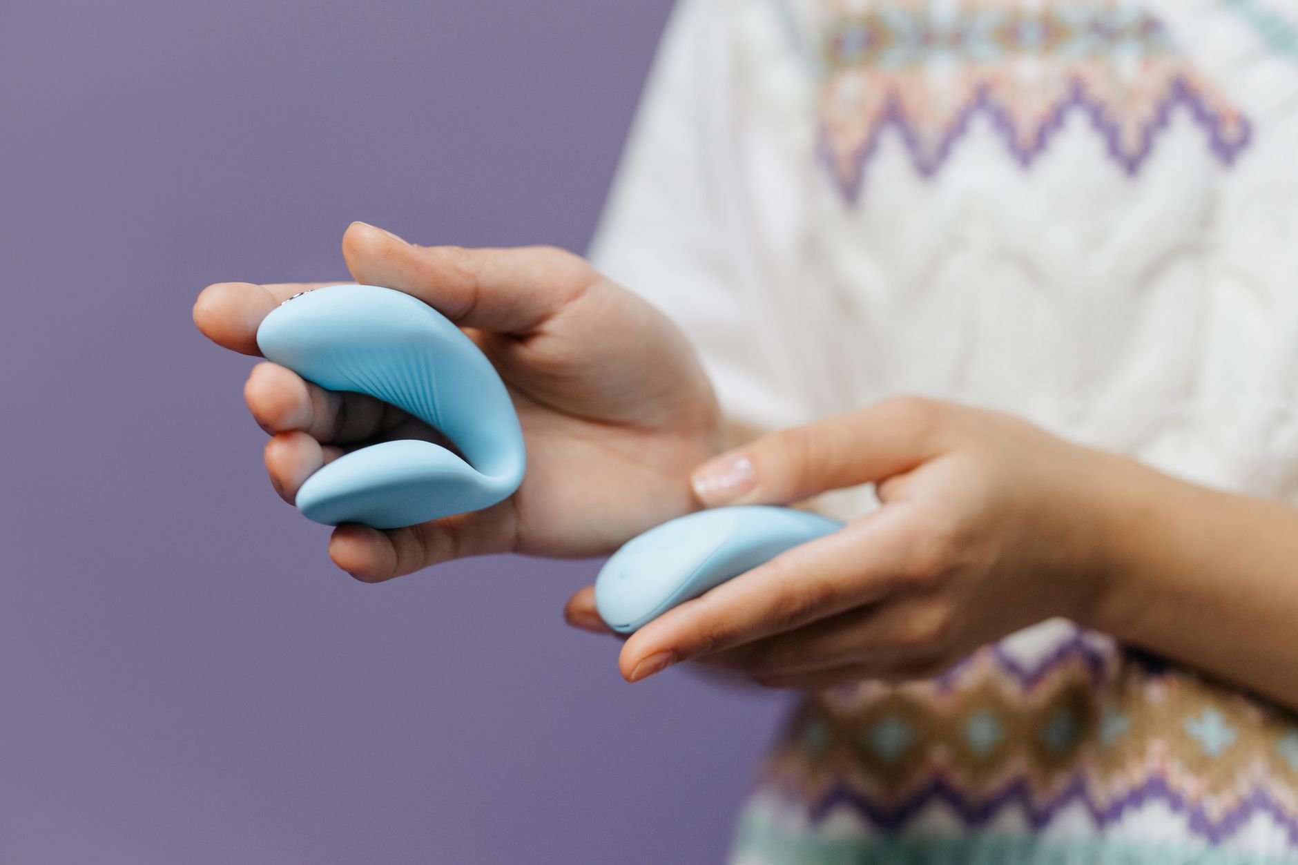 Close-up of a hand holding a sleek blue vibrator against a purple background