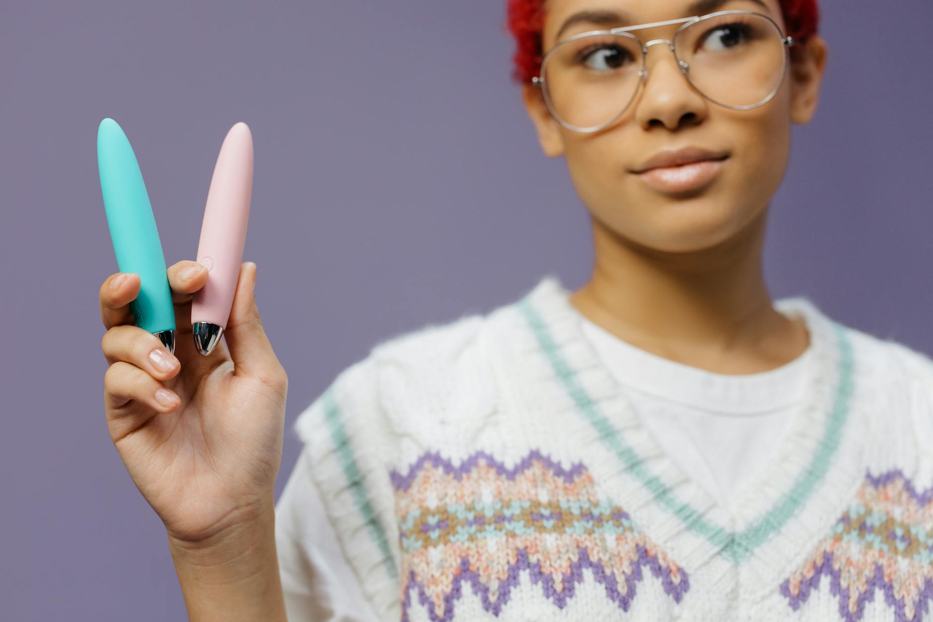 Una mujer joven sostiene vibradores coloridos contra un fondo púrpura