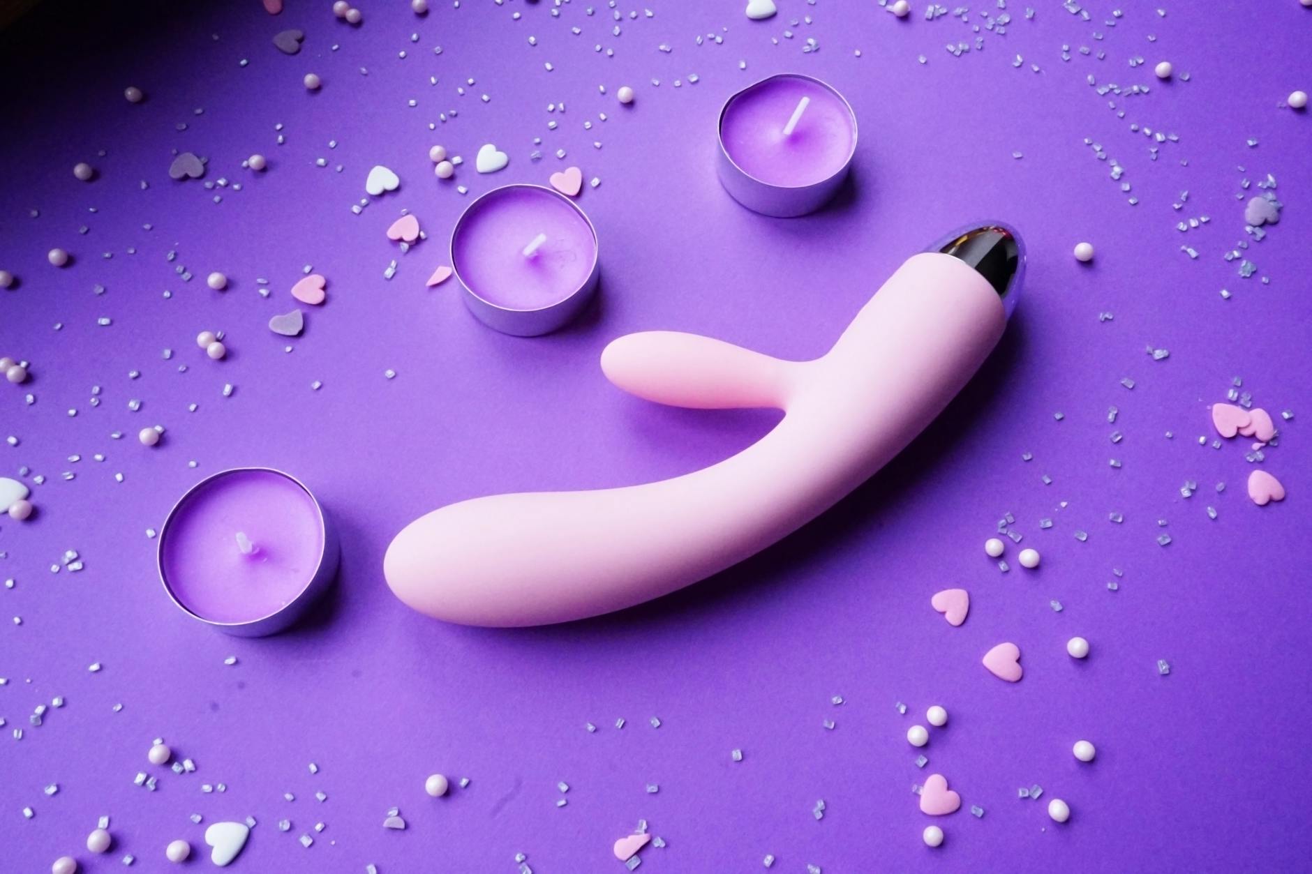 Pink lemon vibrator on purple background with heart confetti and candles for a sensual atmosphere.